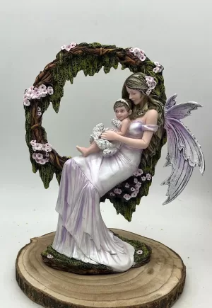 Hada Idía con su bebé en brazos, sentada en un arco de ramas con flores rosas, figura de 35 cm