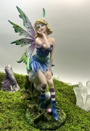 Hada Janel de 27 cm sentada sobre una flor, en tonos pastel azul y lila, con alas verdes y moradas
