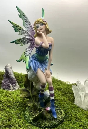 Hada Janel de 27 cm sentada sobre una flor, en tonos pastel azul y lila, con alas verdes y moradas